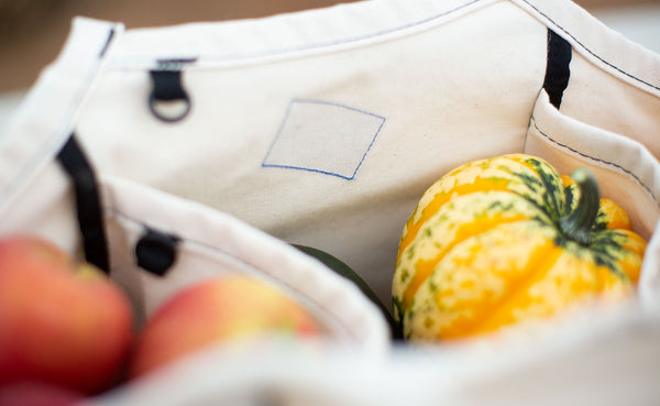The Organic Cotton Truck in Natural; packed with winter squash and apples, this close-up shows the blue thread and stitching of the TOM BIHN moon label.